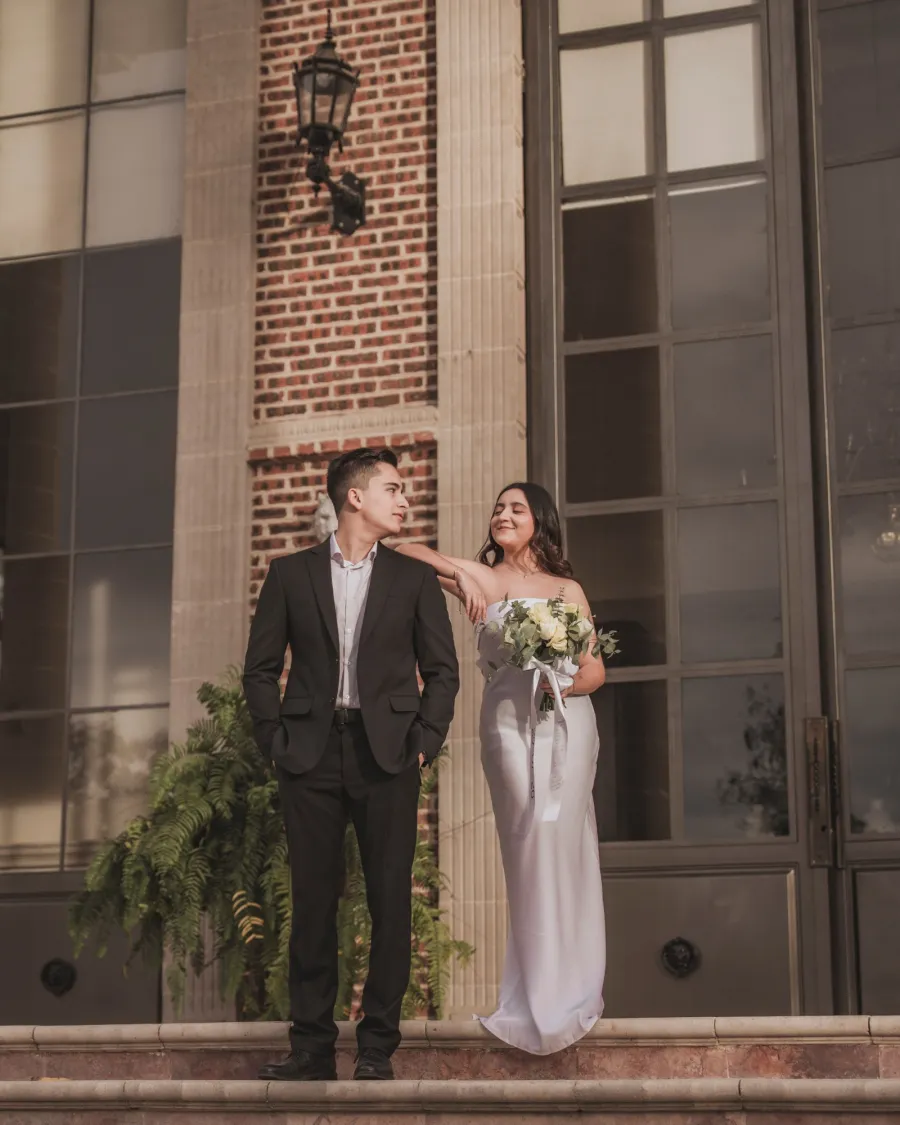 Sesión preboda de luut: pareja en la escalinata de un edificio de ladrillo, ella con su ramo de flores blancas